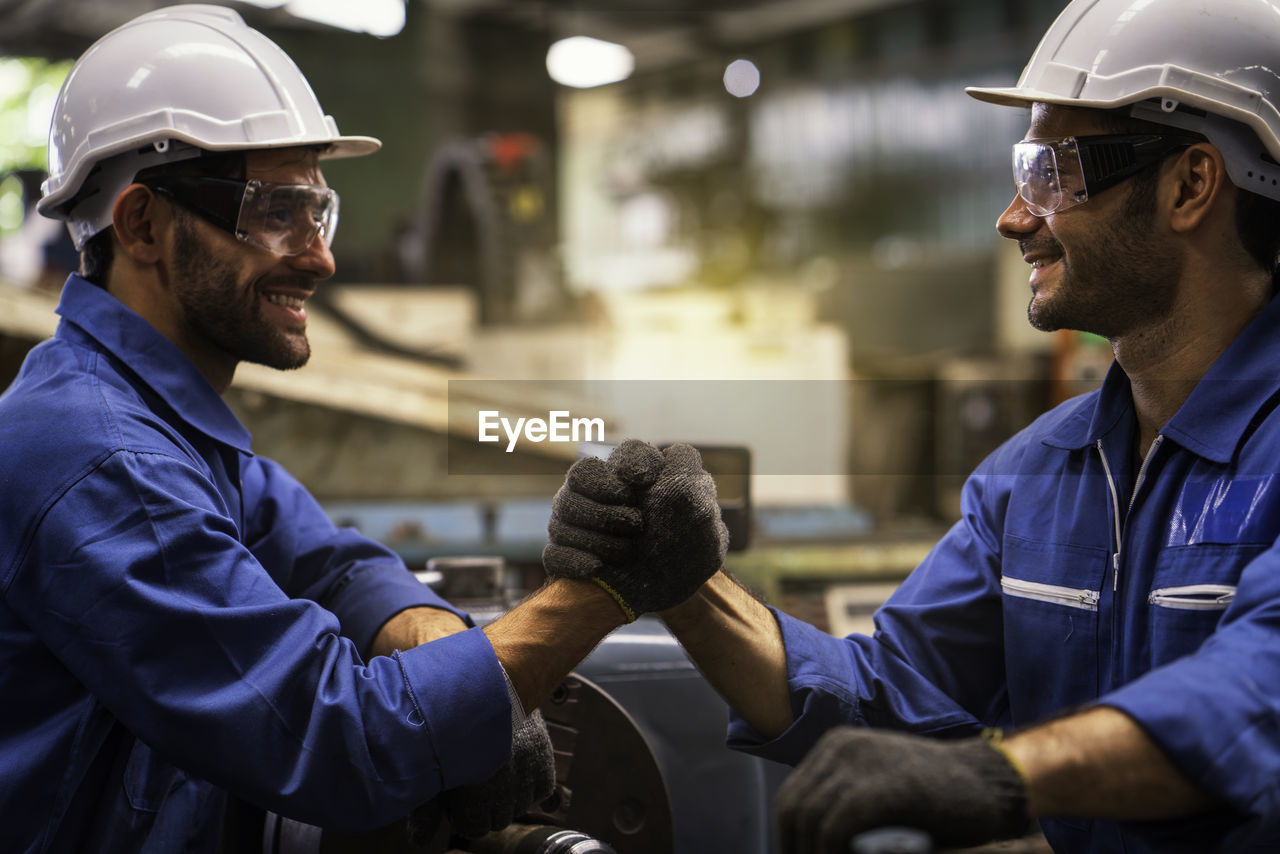 Smiling workers shaking hands while working at factory