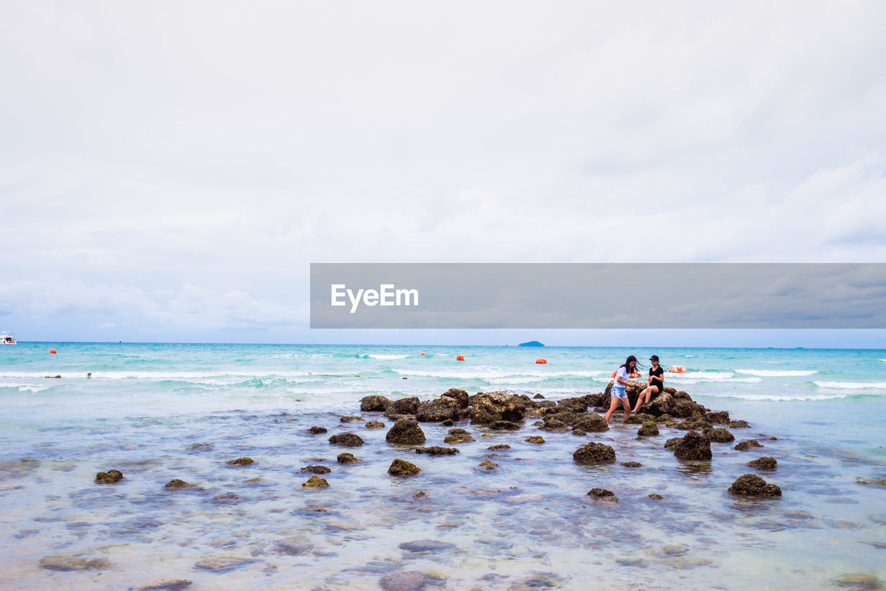 Women sitting on rocks at beach against sky