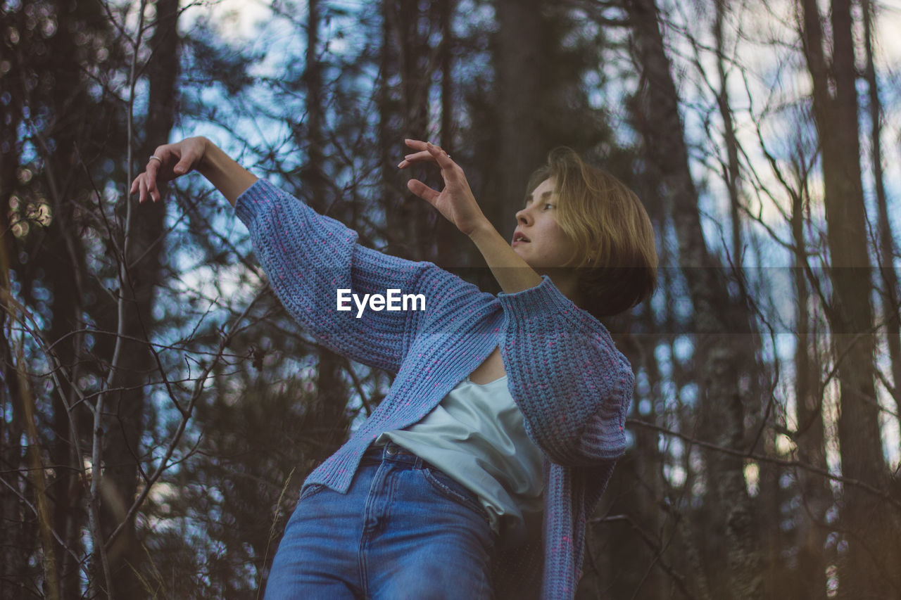 Young woman with short hair dancing against trees in forest