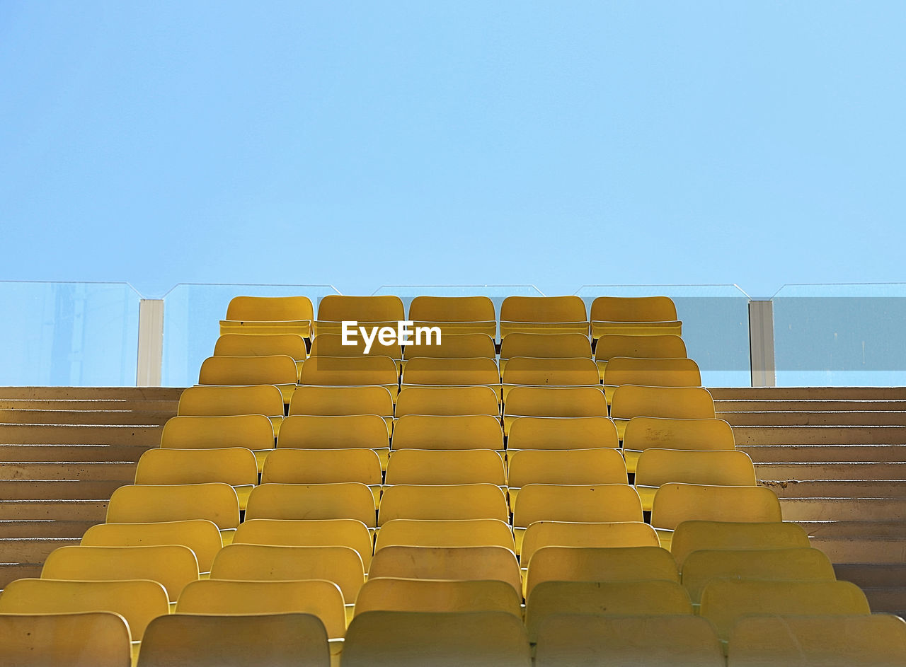 Empty yellow chairs at stadium against clear blue sky