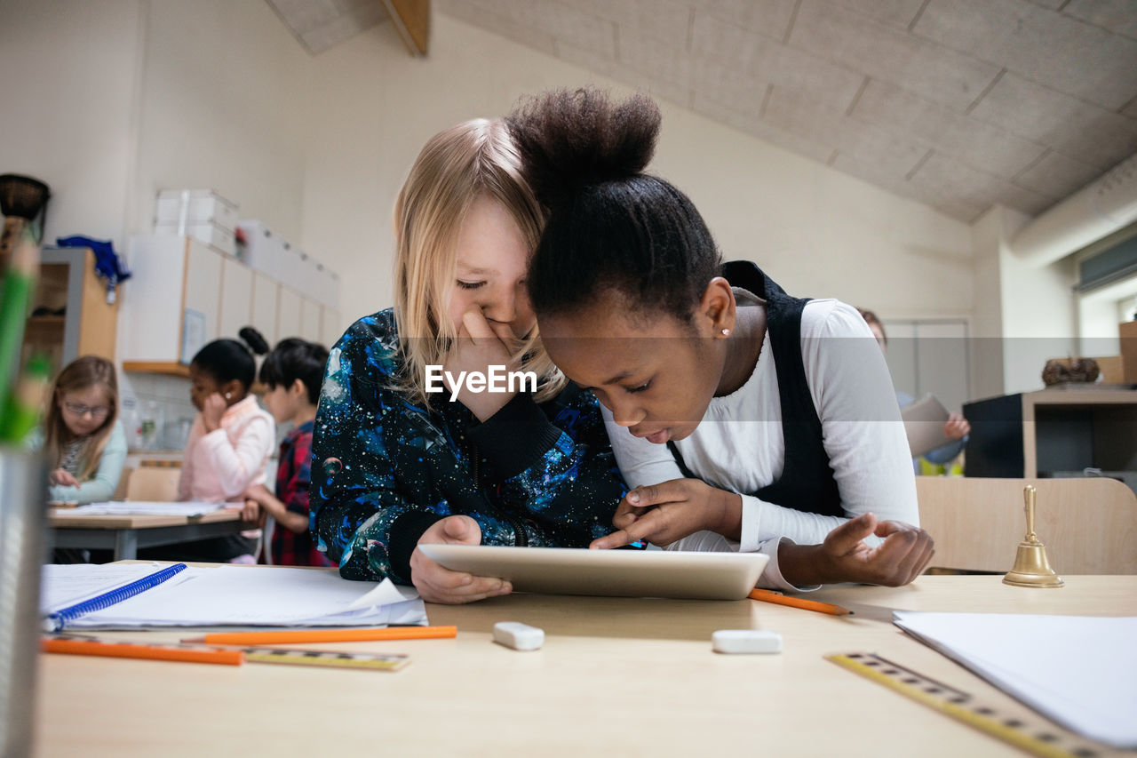 Multi-ethnic students using digital tablet at desk in classroom