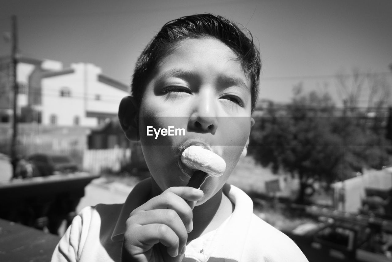 Close-up of boy eating popsicle while standing in city