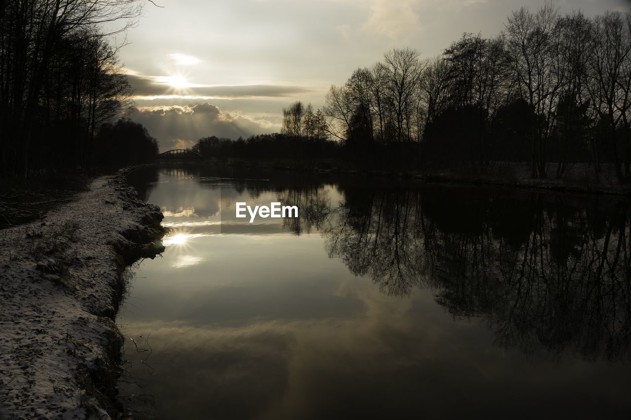 Scenic view of silhouette trees by river against sky