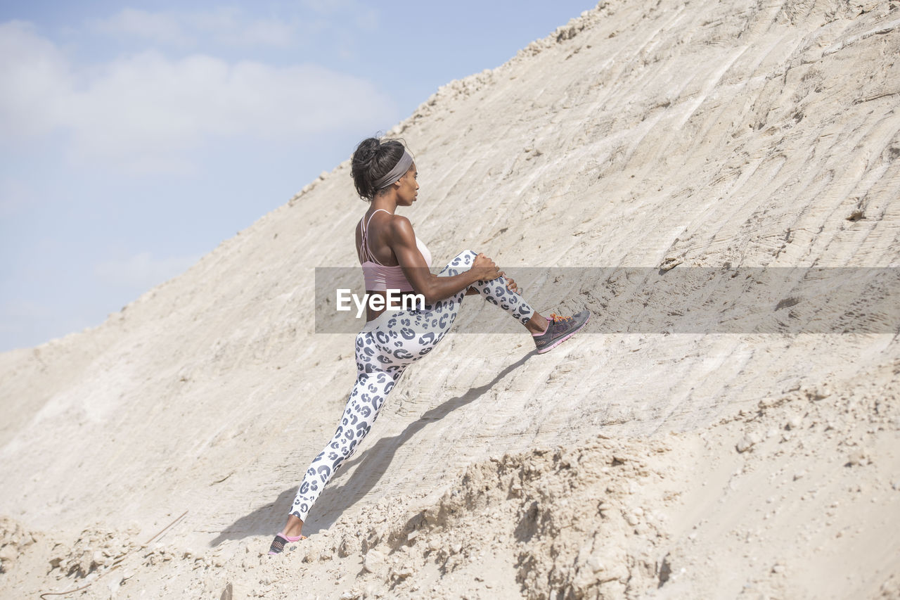 Side view of female athlete exercising rock formation against sky during sunny day