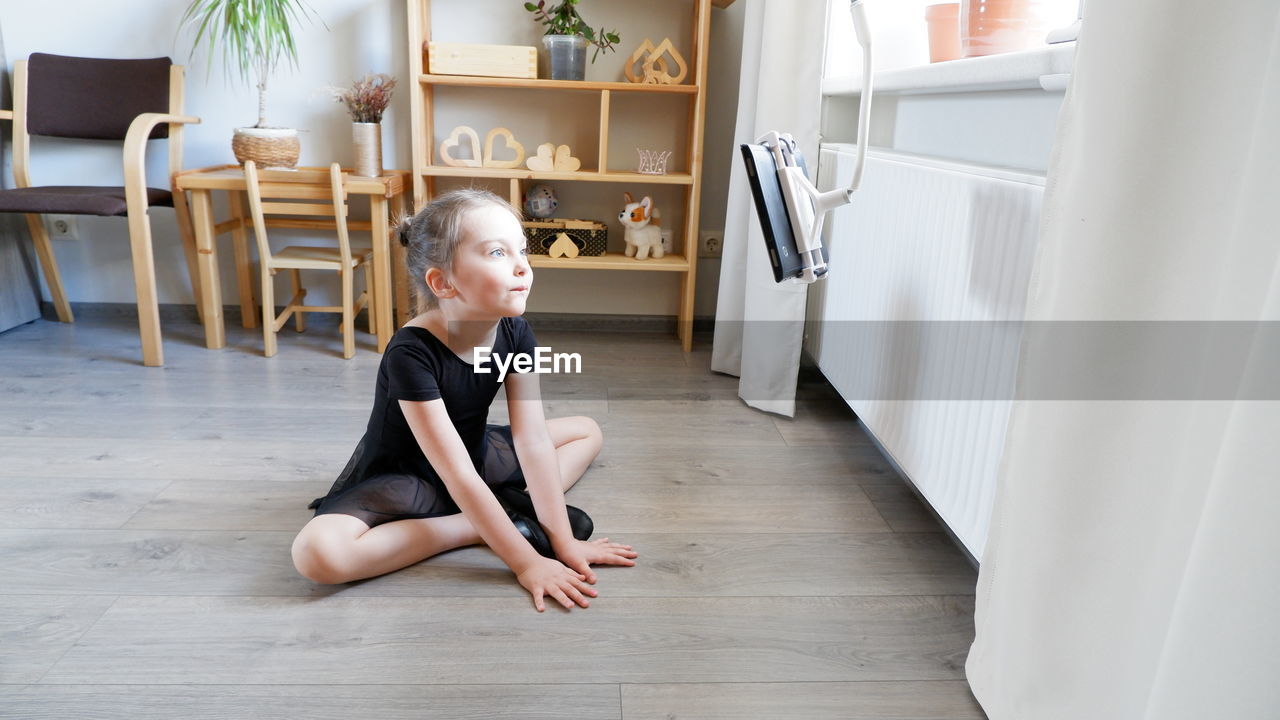 Cute girl looking away while sitting on hardwood floor at home