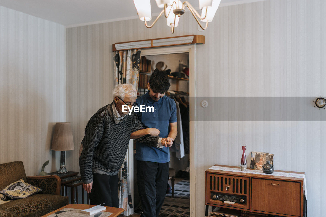 Male caregiver holding hands of senior man while walking at home