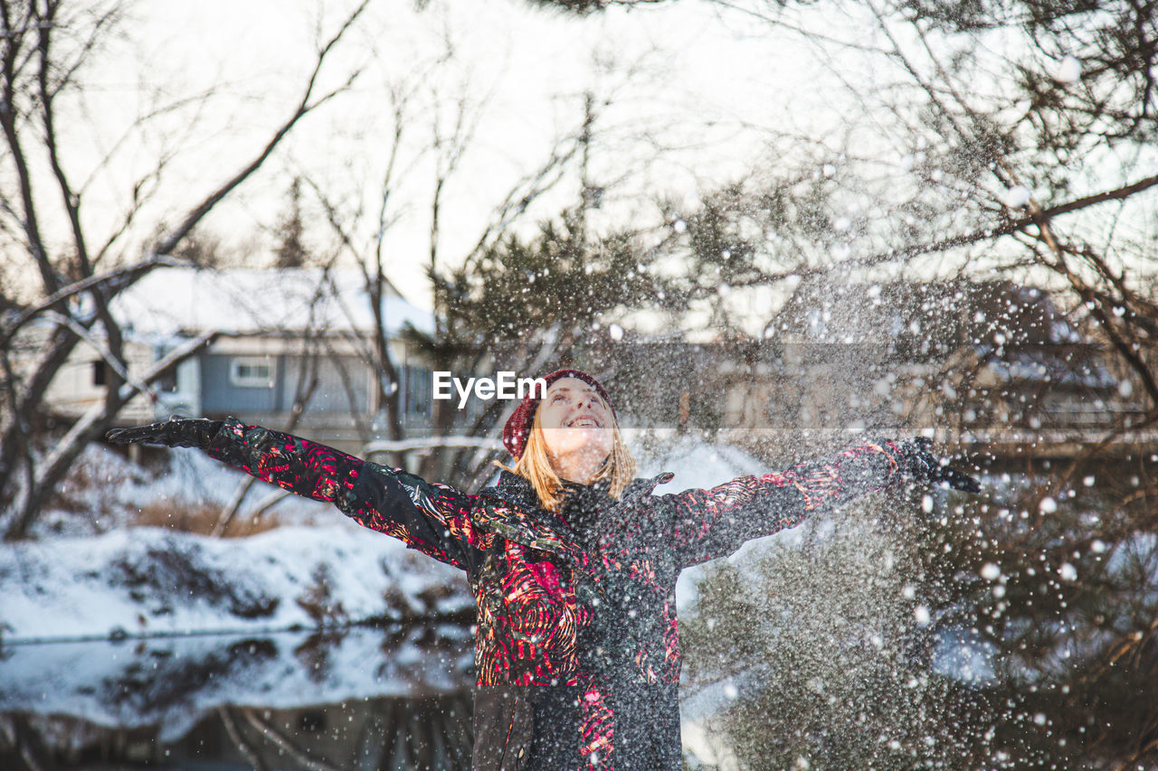 Smiling young woman throwing snow mid air during winter