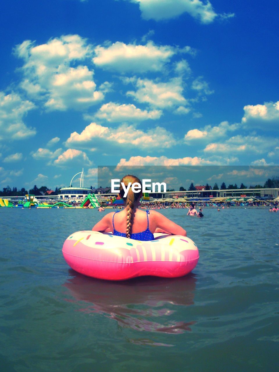 Rear view of young woman sitting in inflatable ring on sea against sky during sunny day
