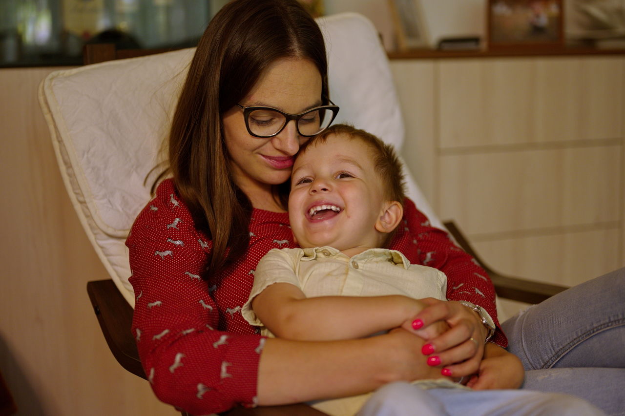 Mother sitting in armchair and holding her cute little toddler