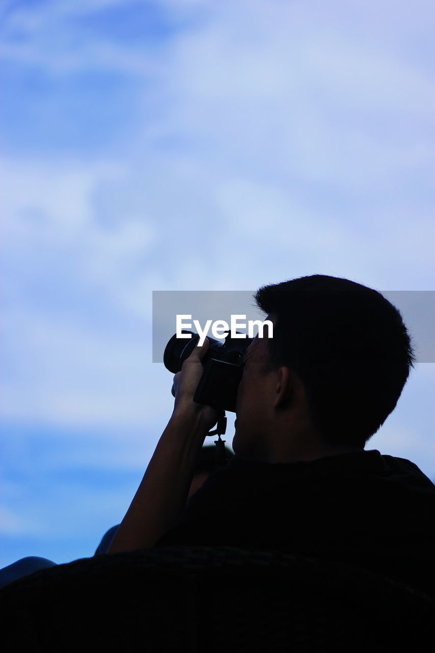 Low angle view of man photographing against sky