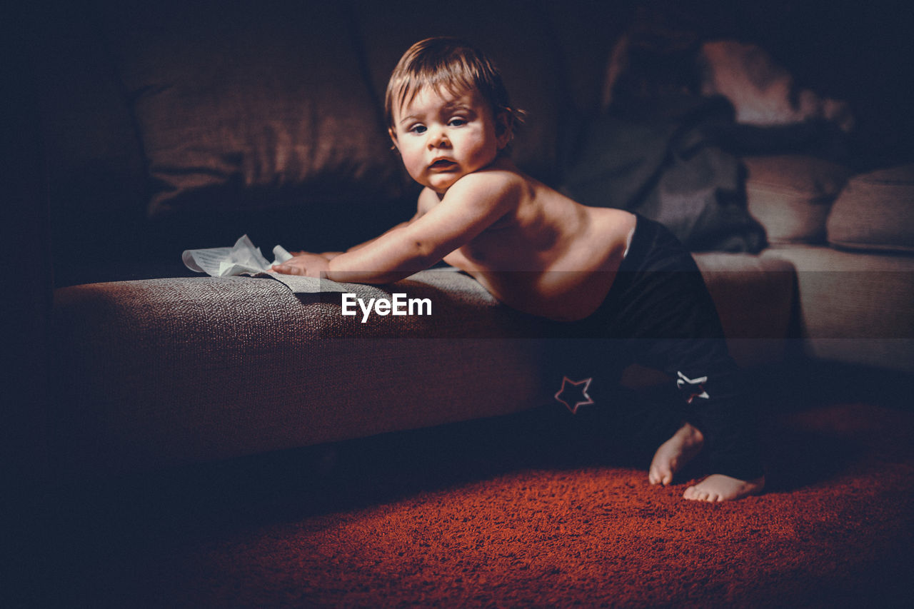 Portrait of shirtless baby boy standing by sofa at home