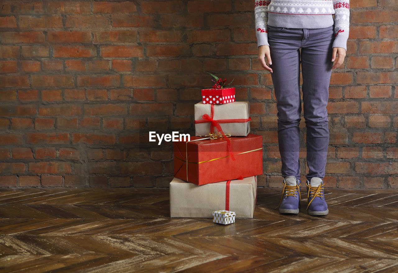 LOW SECTION OF WOMAN STANDING ON RED BRICK WALL