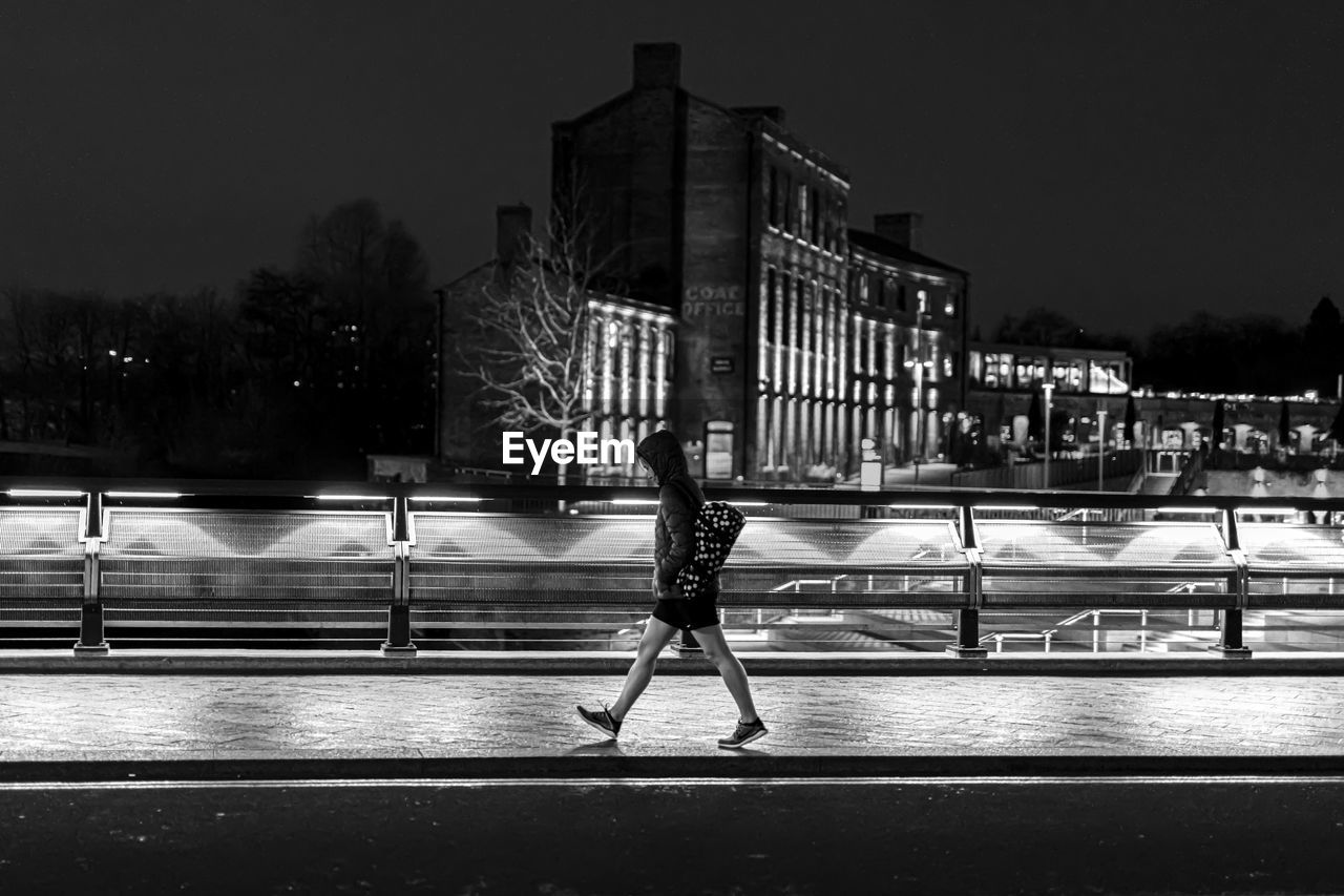 BLURRED MOTION OF MAN ON ILLUMINATED STREET AGAINST BUILDINGS IN CITY