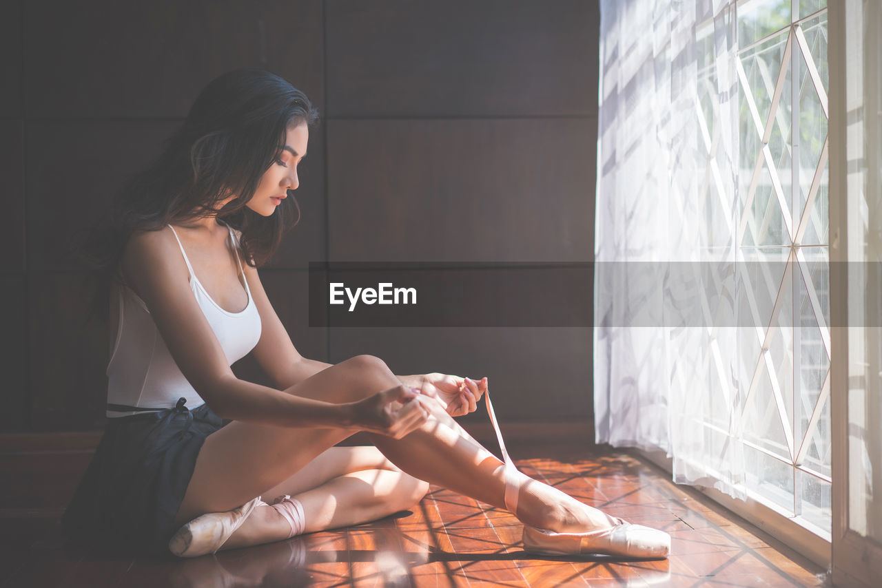 Young woman wearing shoe while sitting on floor