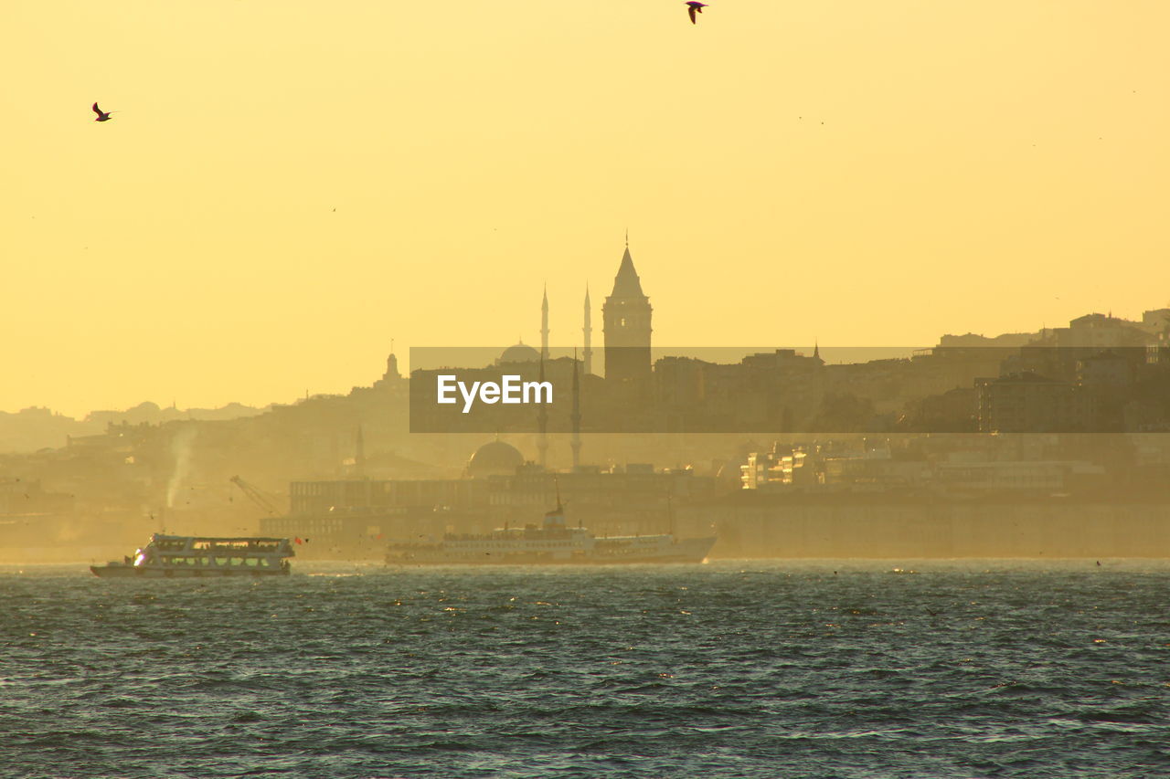 Passenger crafts sailing in strait by galata tower against clear sky during sunset