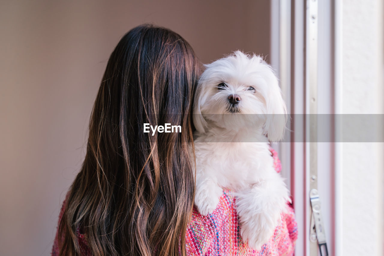 Rear view of woman with dog standing at home