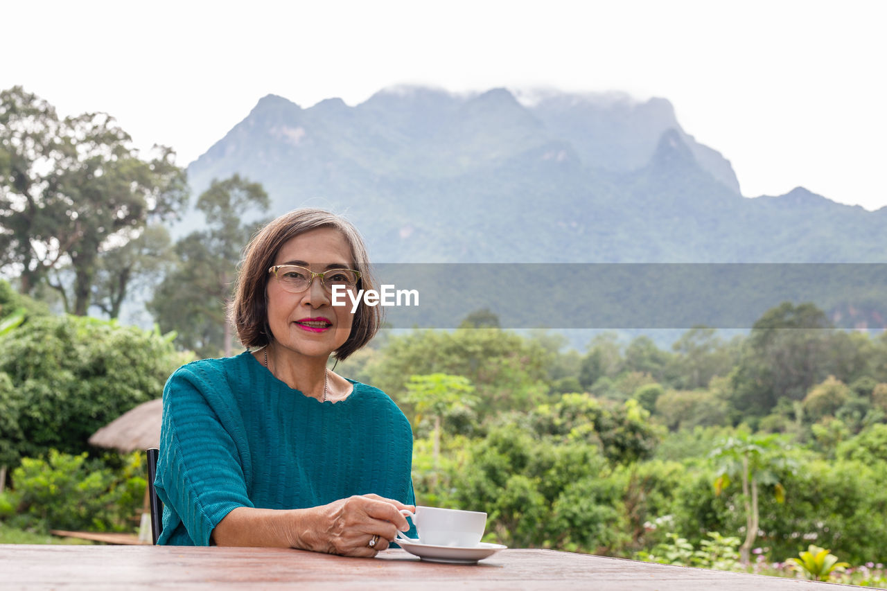 Asin senior woman drinking coffee in cafe outdoor with mountain view