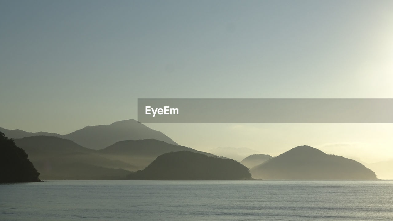 Scenic view of sea and mountains against clear sky