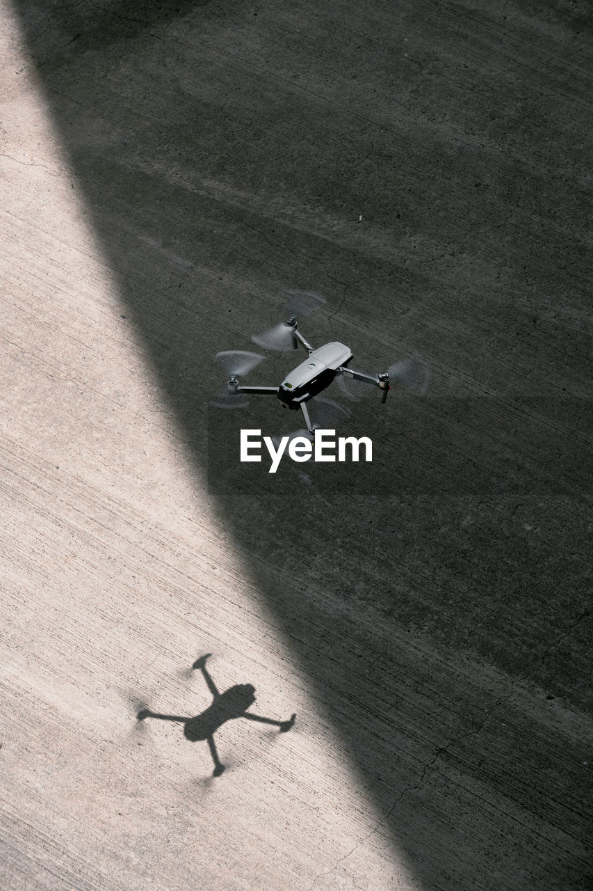 From above modern drone flying in empty concrete walkway casting shadows on sunny day