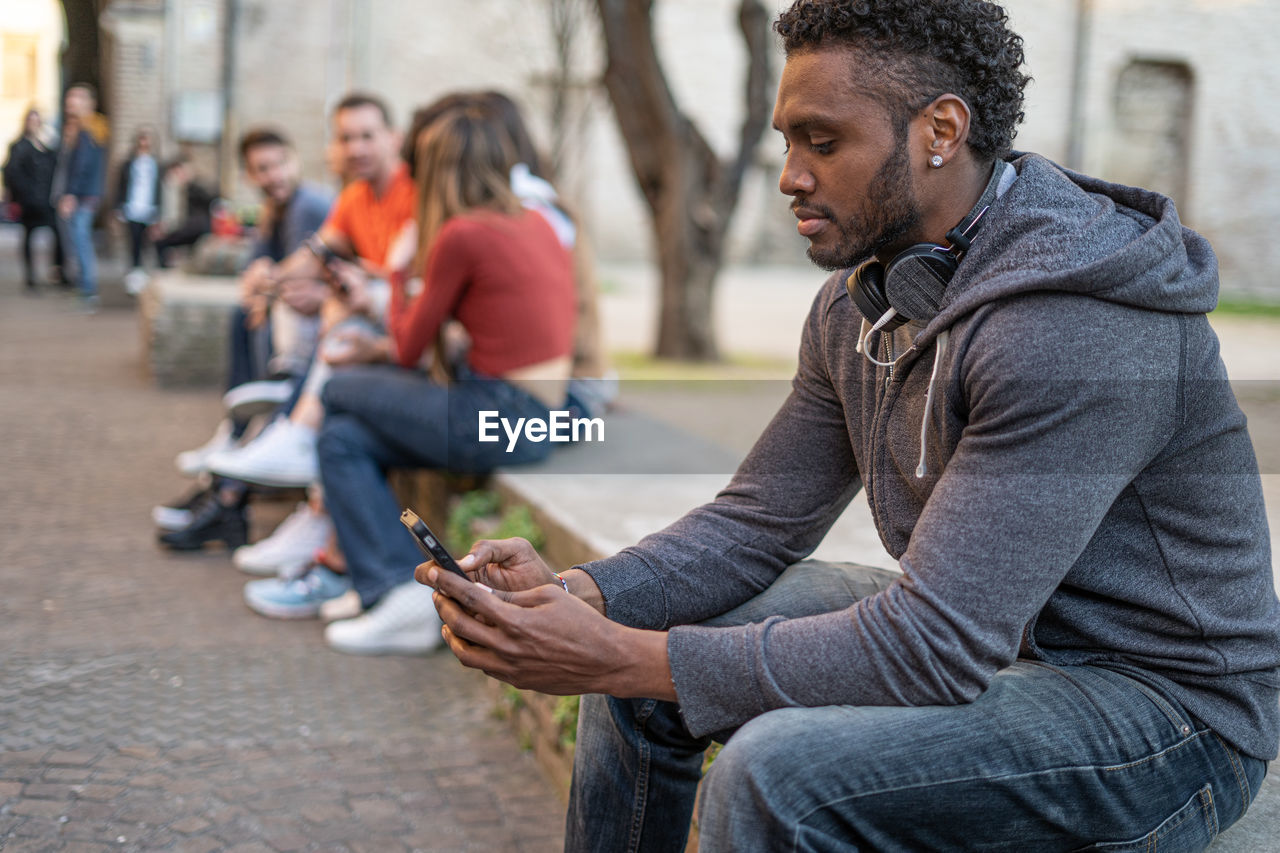 Young man using mobile phone while sitting in city