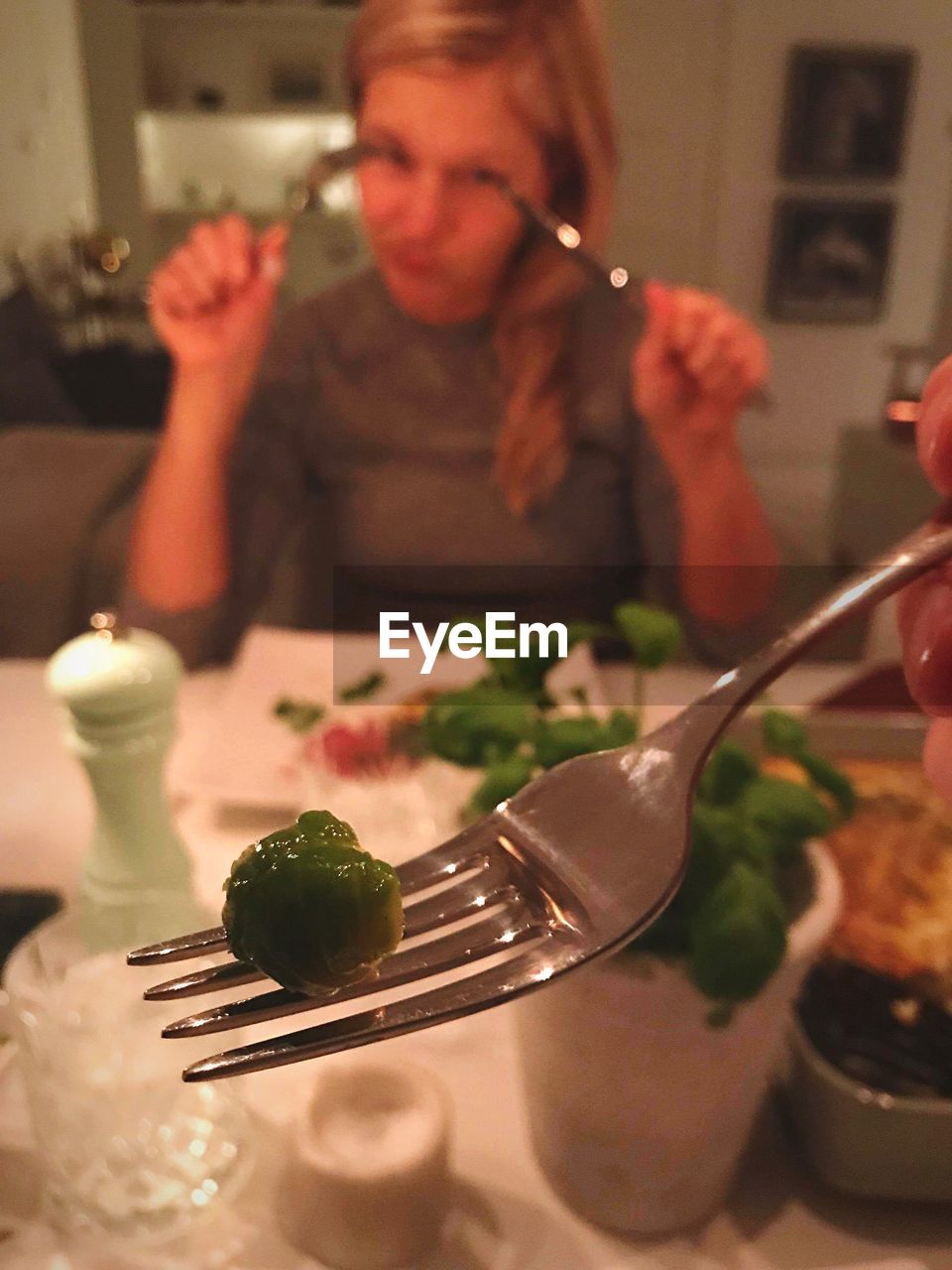 Close-up of green pea on fork against woman sitting at table