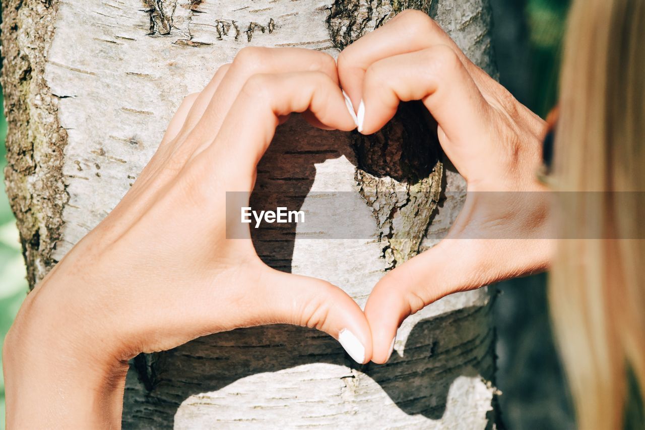 Midsection of woman making heart shape on tree trunk