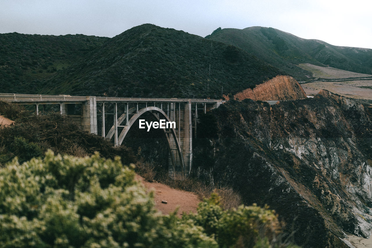 Arch bridge by mountains against sky