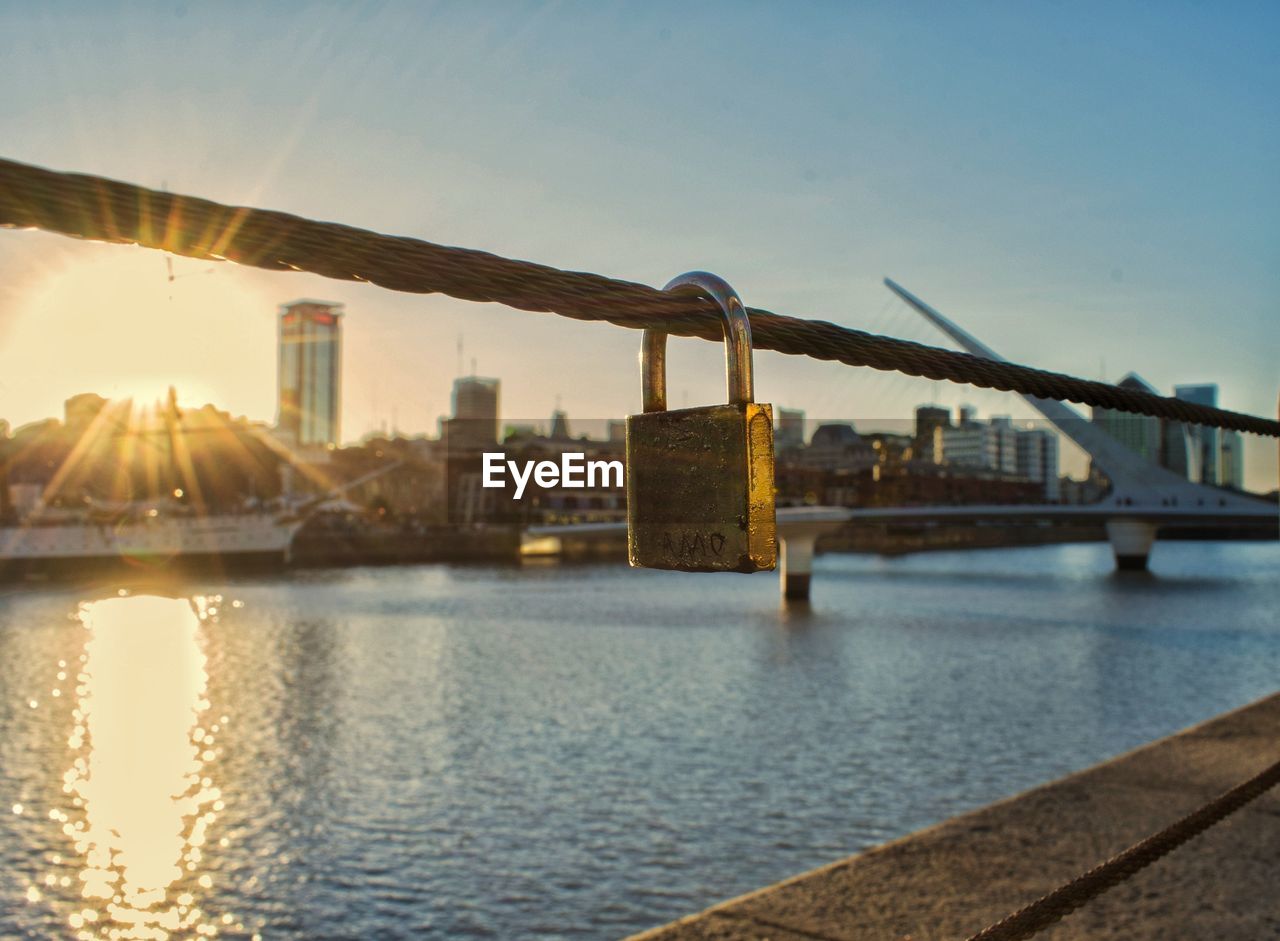 Bridge over river by buildings against sky during sunset