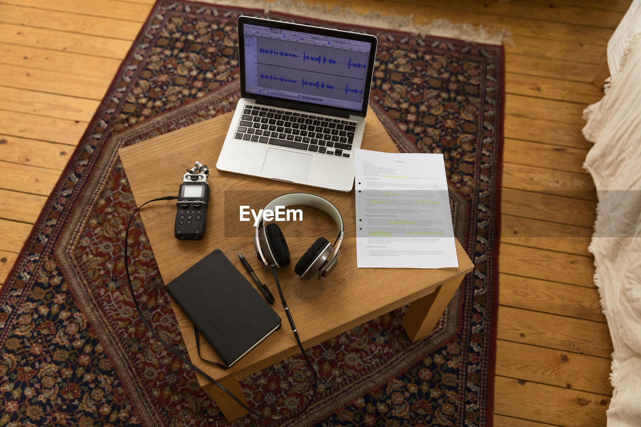 From above of audio recorder and headphones placed on wooden table with laptop and notebook for recording podcast at home