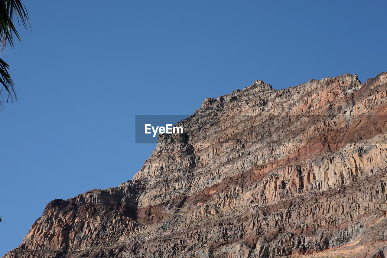 Low angle view of rocky mountain against clear blue sky