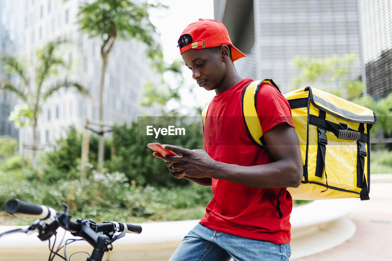 Young delivery man using smart phone while sitting on bicycle