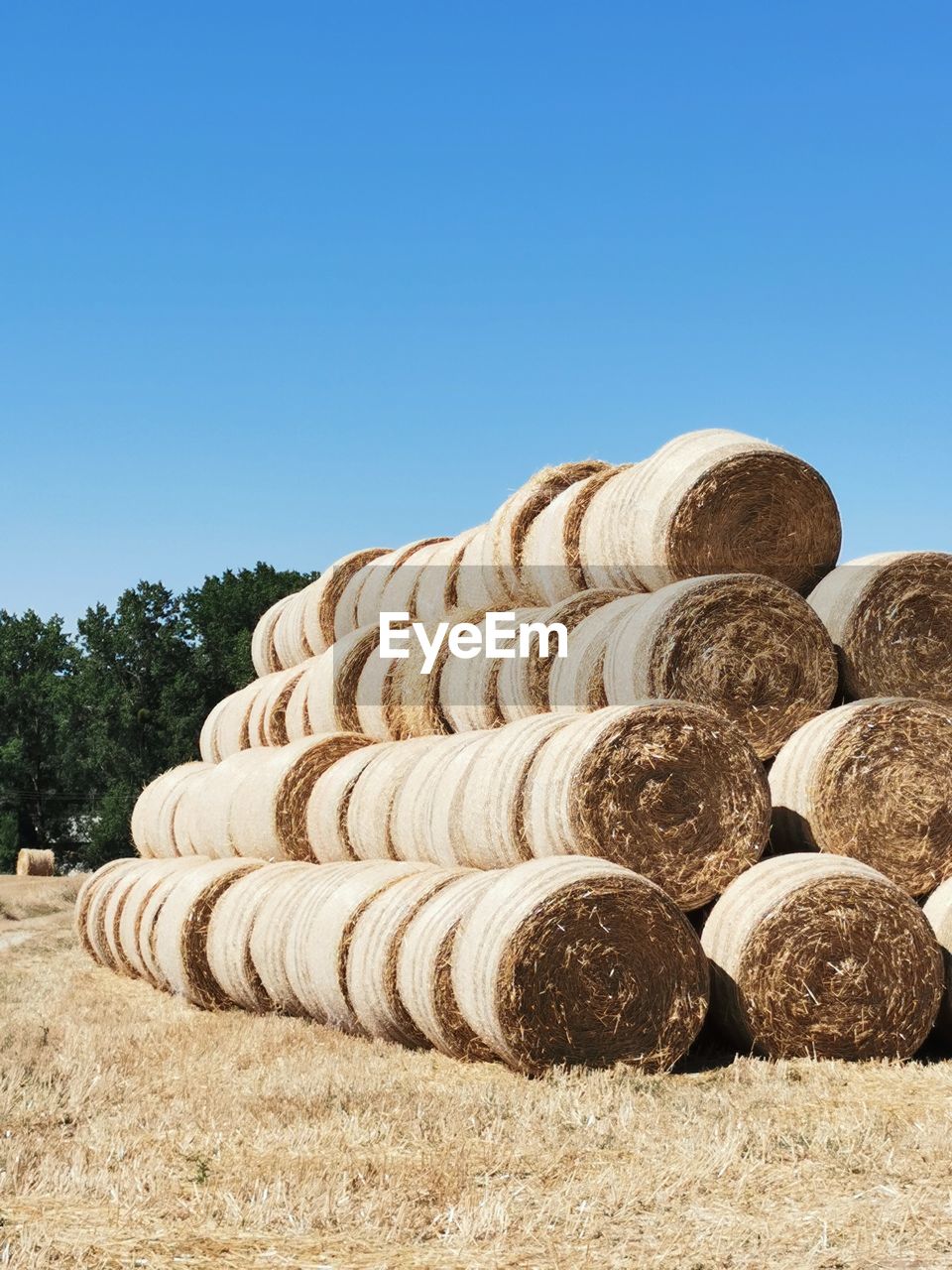 Stack of hay bales on field against clear blue sky