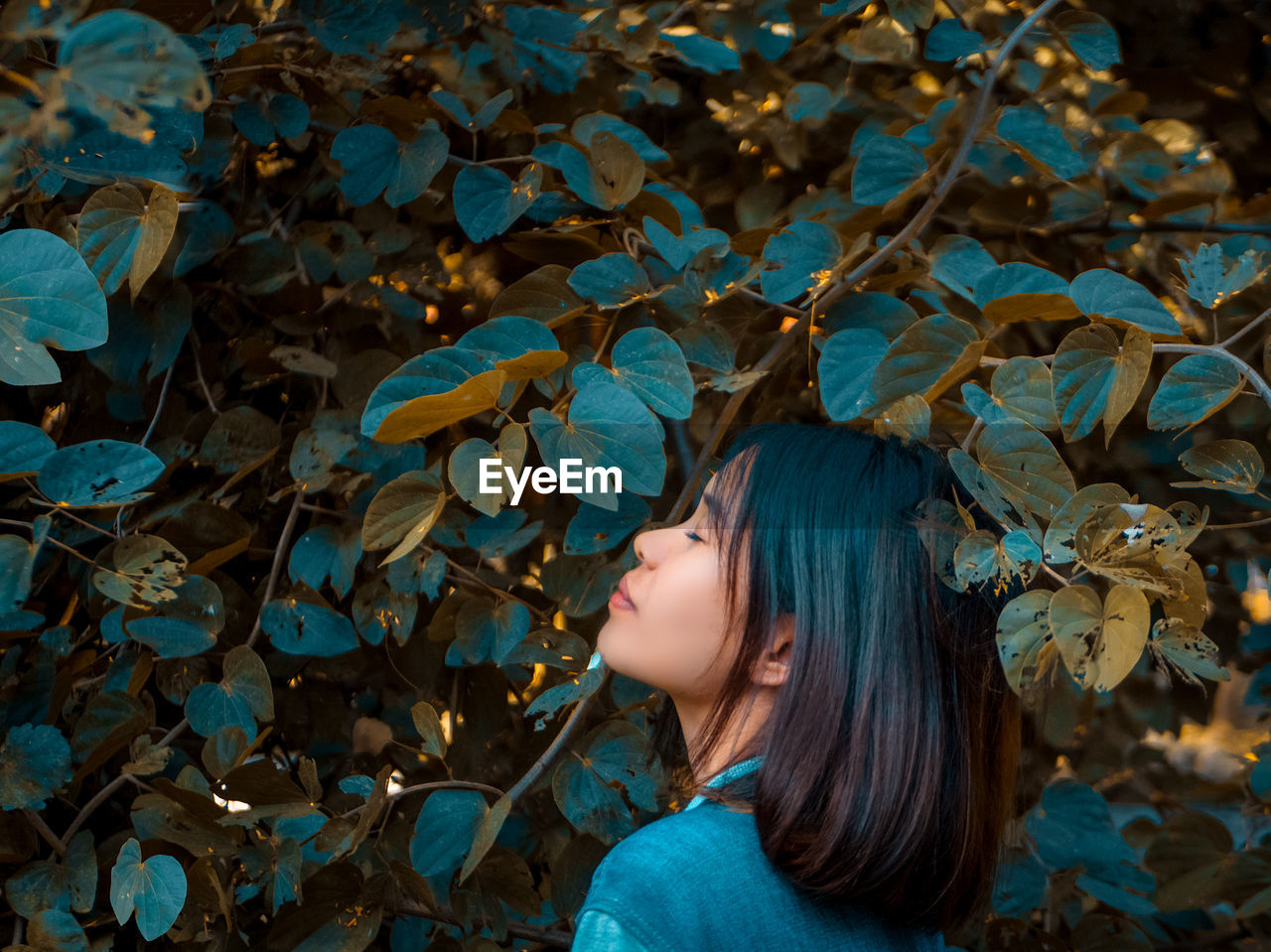 Side view of young woman standing with eyes closed by plants