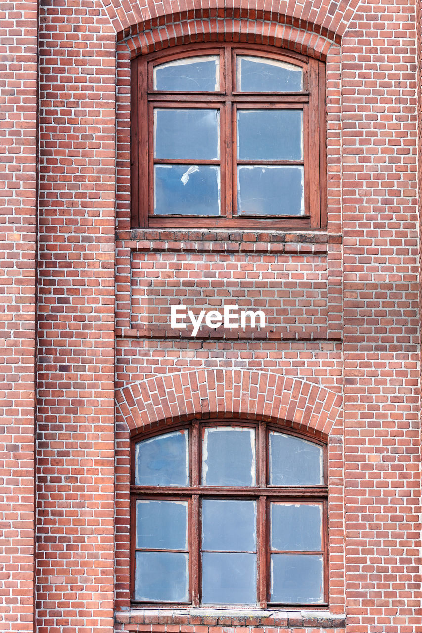 Two arched glass windows set in red brick wall. windows in brown wooden frames on red brick wall