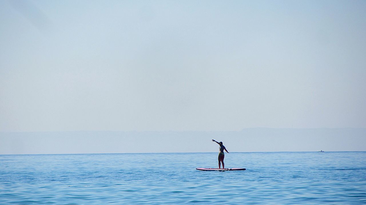 Woman in bikini surfing on sea against clear sky