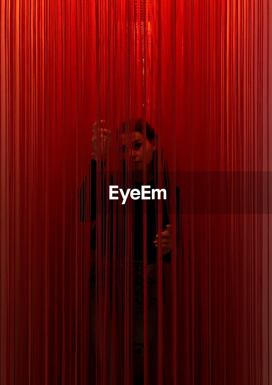 Portrait of woman standing amidst red curtain