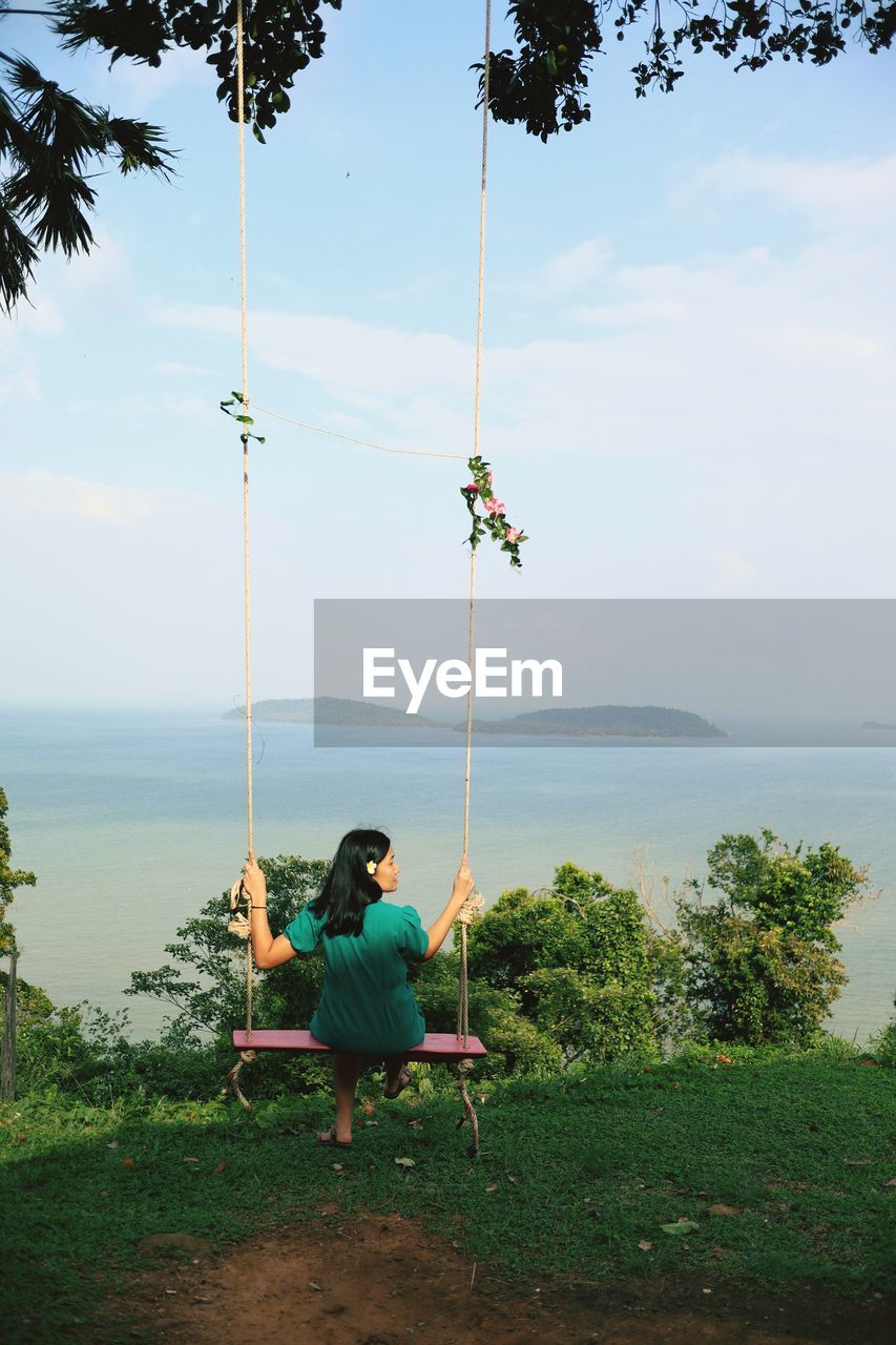 Man sitting on swing in sea against sky