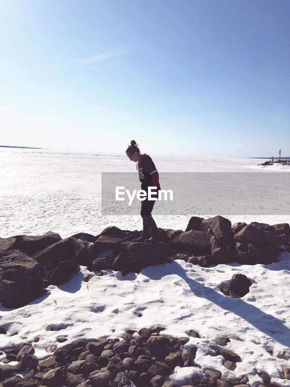Side view of woman standing on rock by froze sea against sky