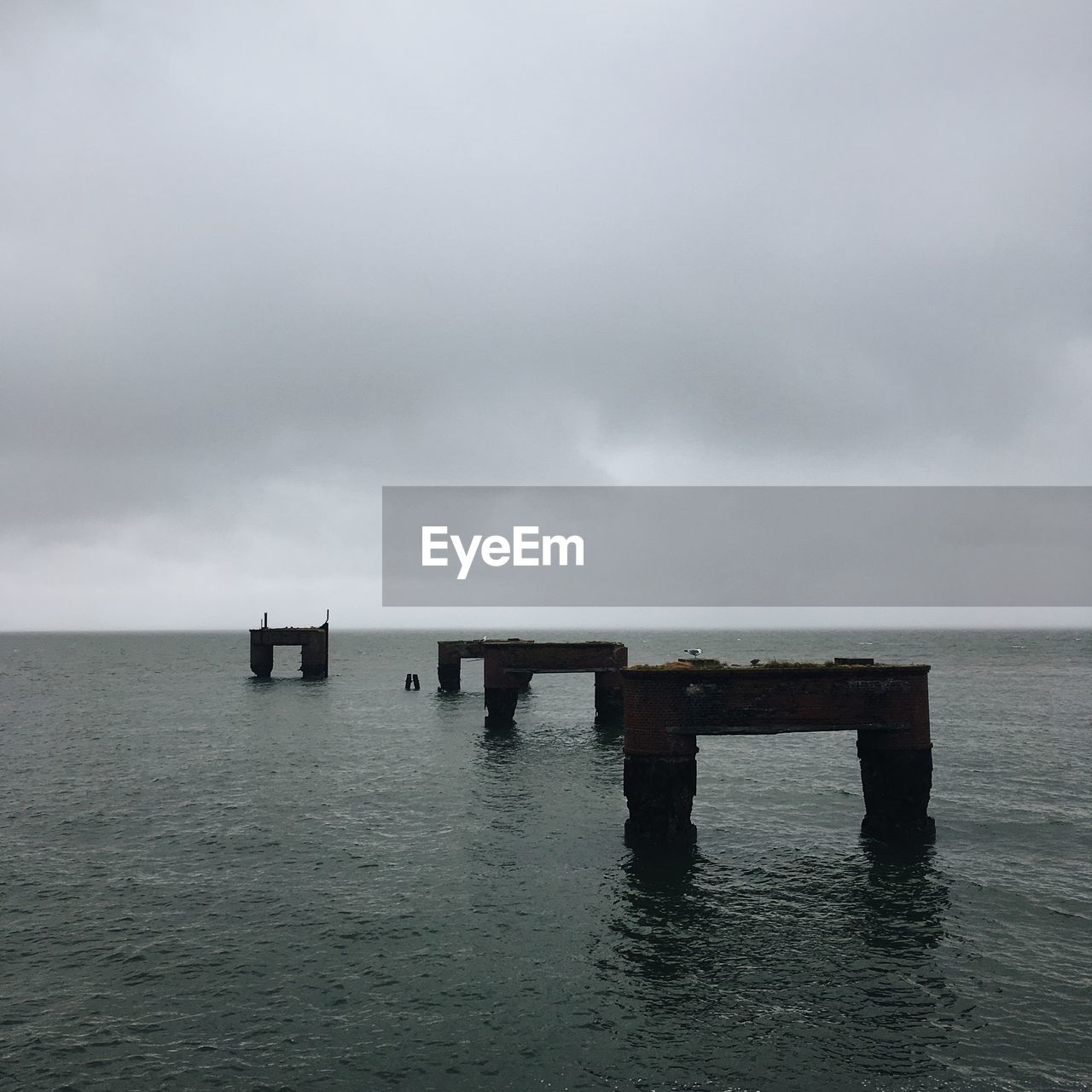WOODEN POSTS ON PIER OVER SEA AGAINST SKY