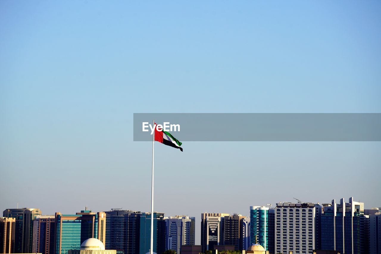 Flag against buildings in city against clear blue sky