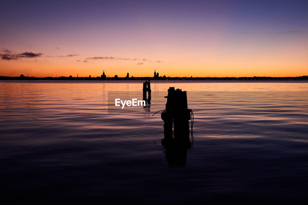 water, sky, sunset, reflection, silhouette, horizon, dawn, sea, beauty in nature, nature, evening, scenics - nature, tranquility, tranquil scene, orange color, cloud, transportation, afterglow, outdoors, men, idyllic, ocean, beach, fishing, nautical vessel, shore, sunlight, horizon over water, environment, sun, land, one person, wave, landscape, non-urban scene, travel destinations, travel, holiday, leisure activity, lifestyles