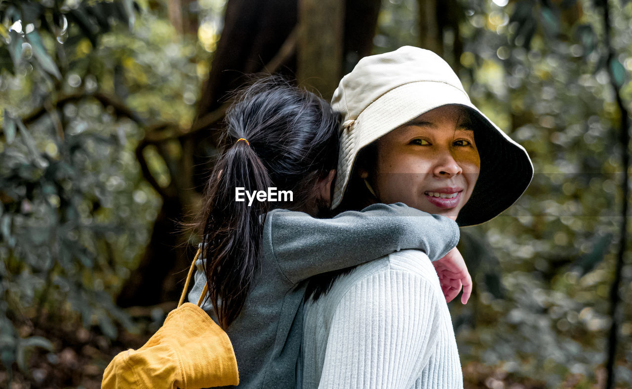 Portrait of smiling mother carrying daughter on back in forest