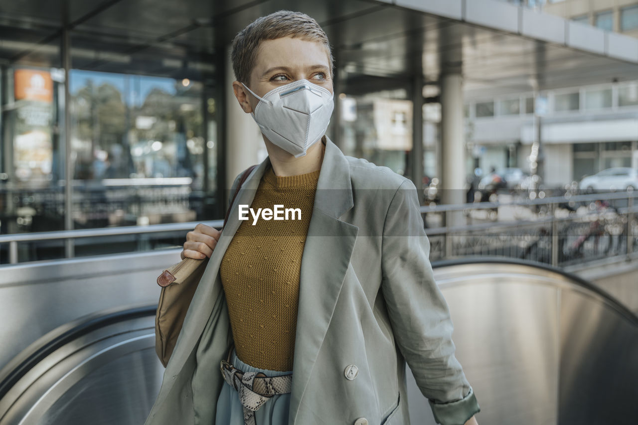 Woman wearing protective face mask looking away climbing on escalator in city