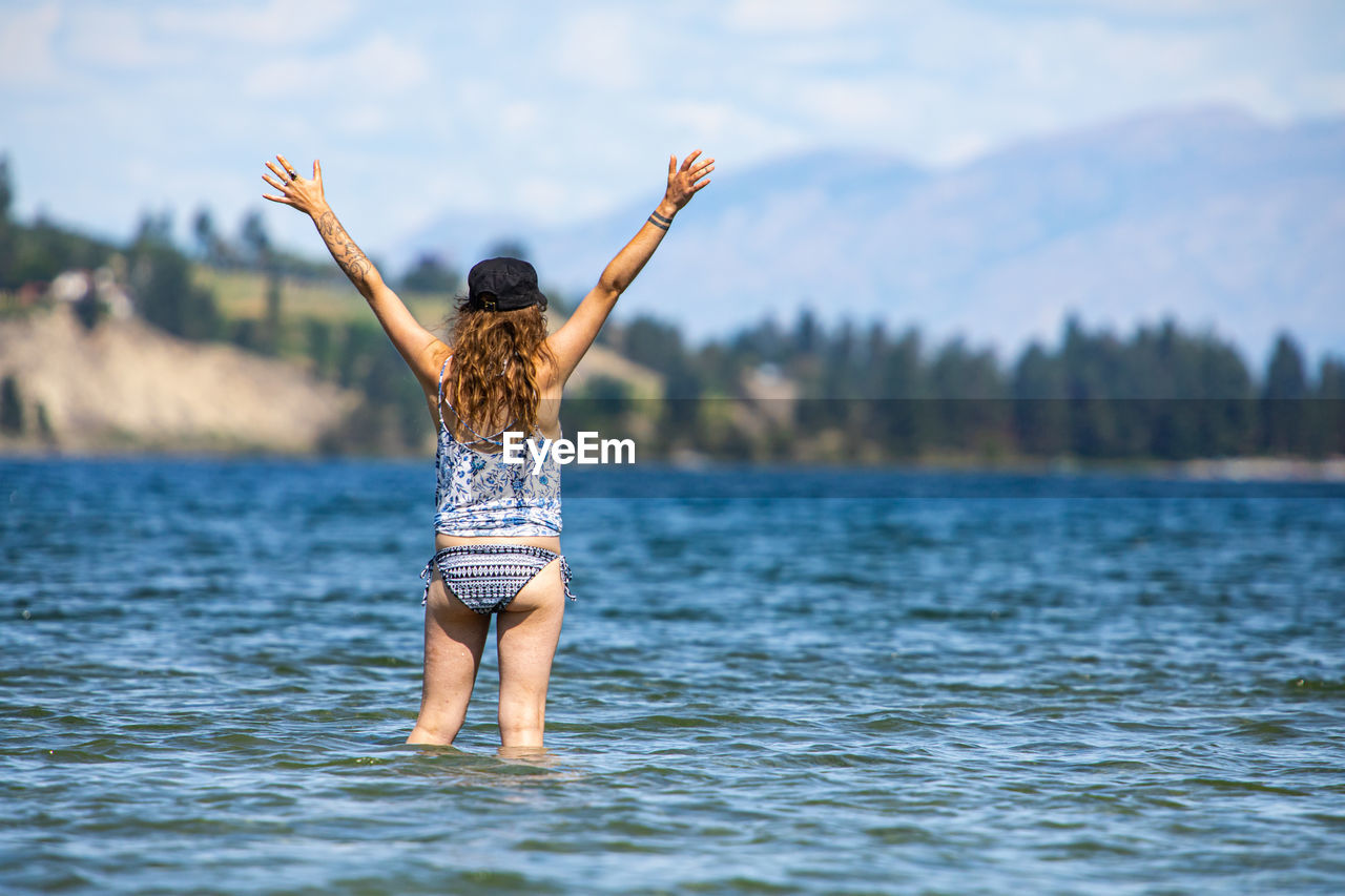 Rear view of woman with arms raised in lake