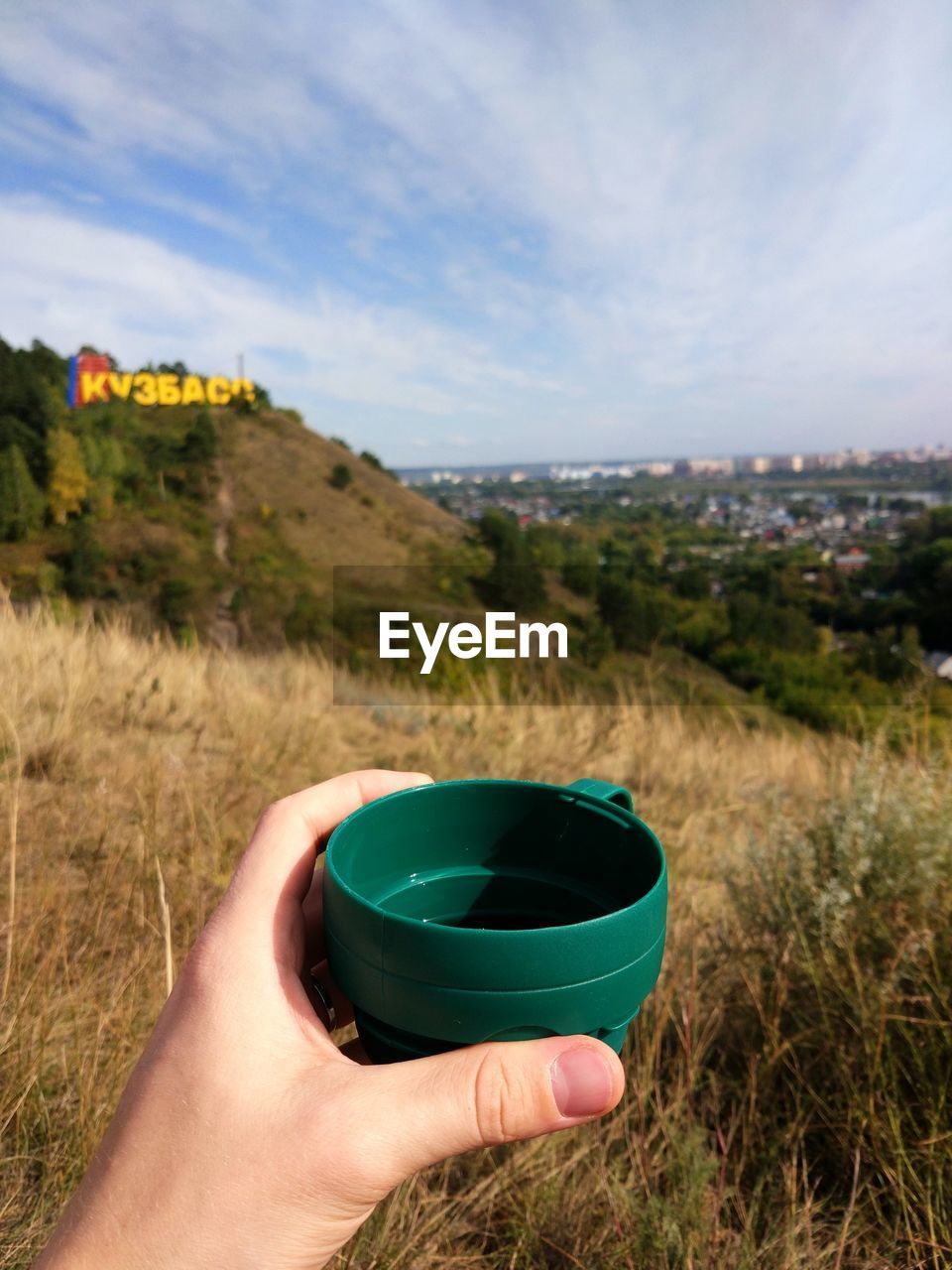 MIDSECTION OF PERSON HOLDING SUNGLASSES ON LANDSCAPE