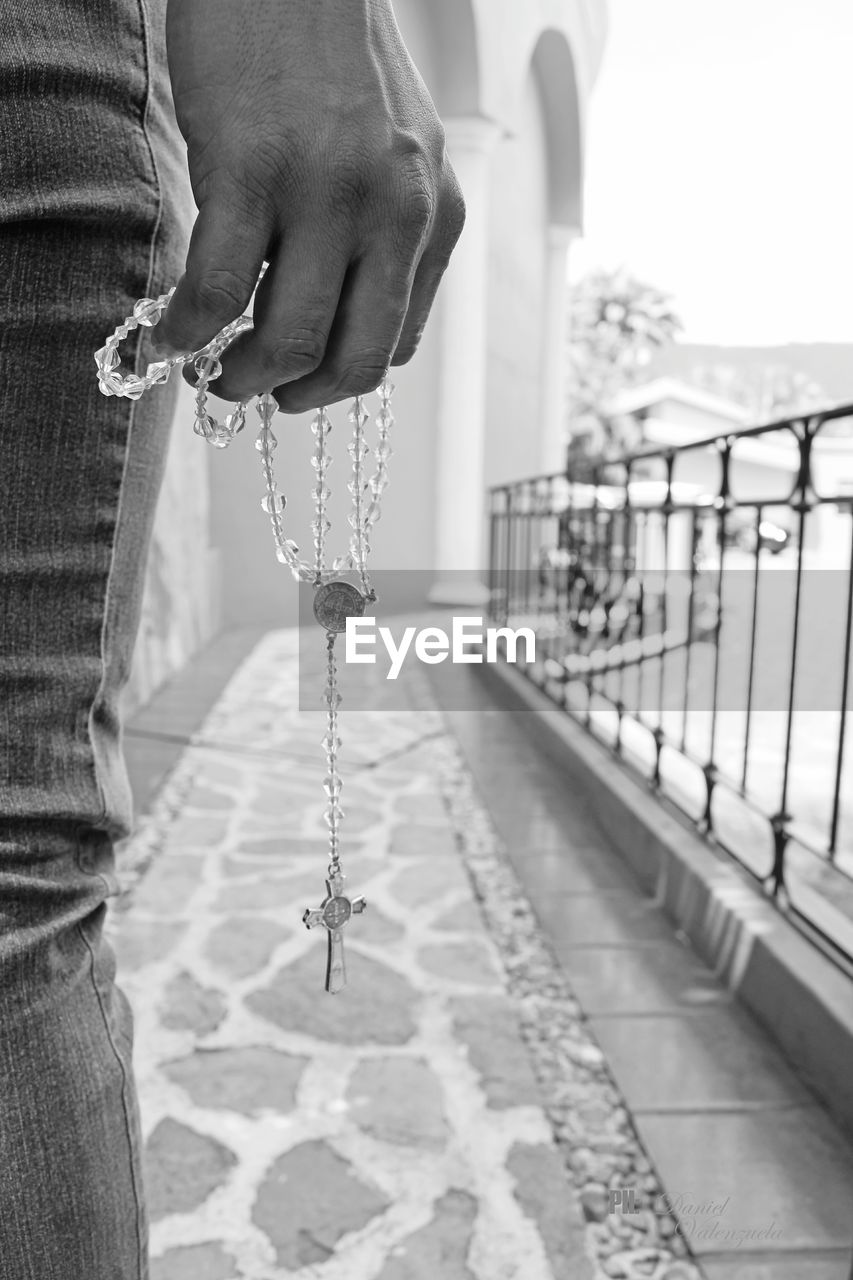 Midsection of person holding rosary beads on footpath