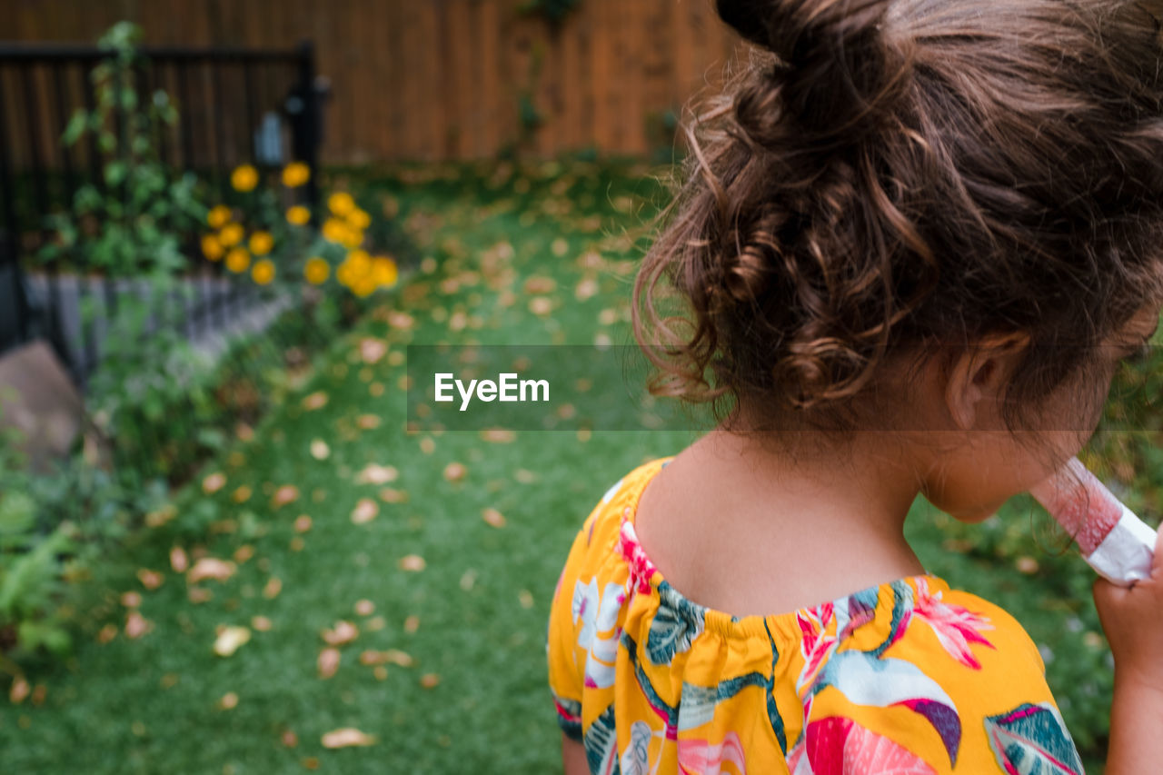 Little girl with curly hair eating a popsicle outside