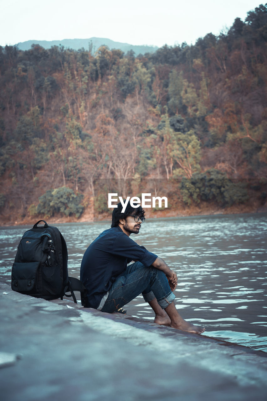 Young man sitting on rock by lake