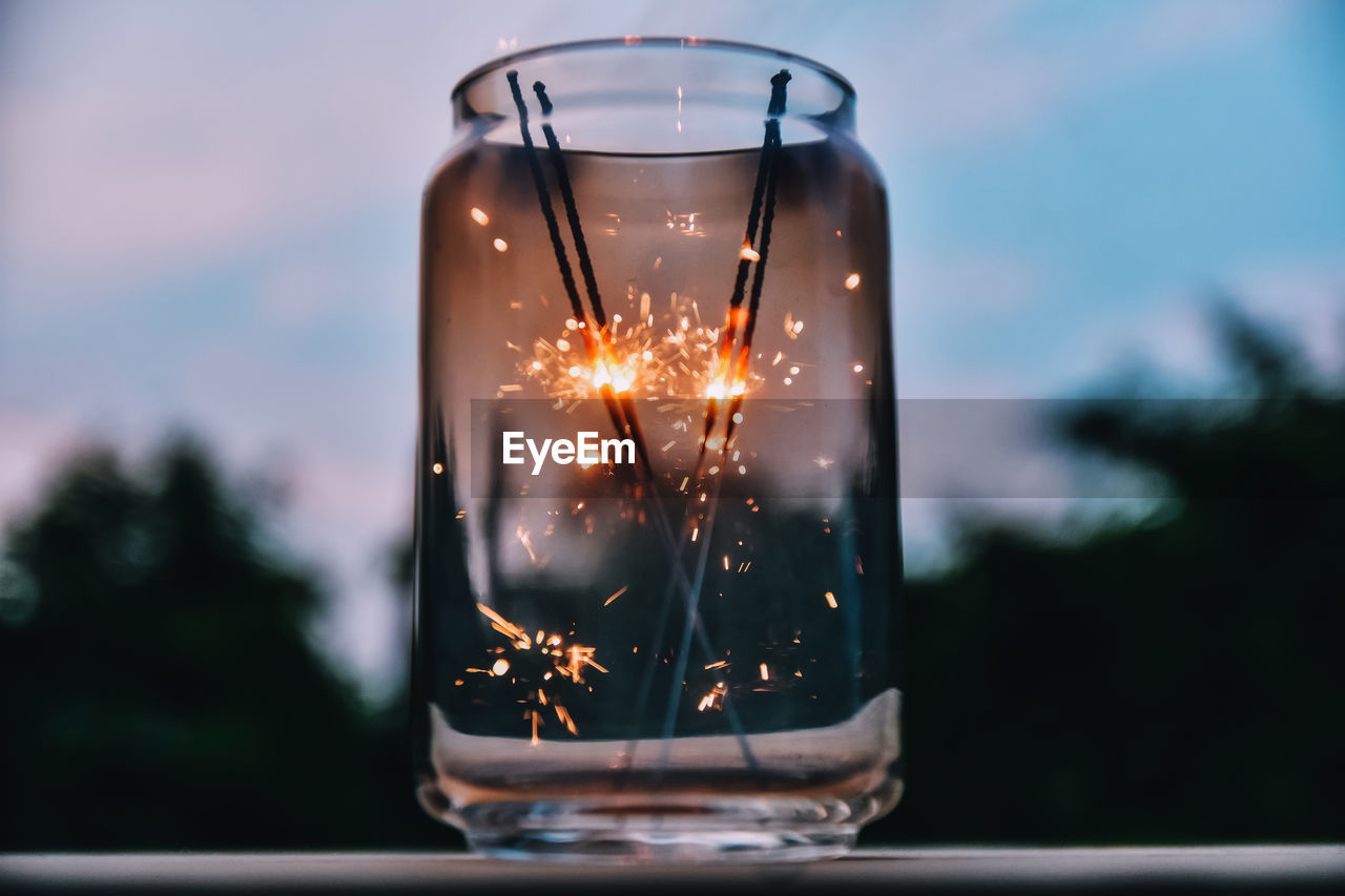 Close-up of sparklers burning in jar on table against sky