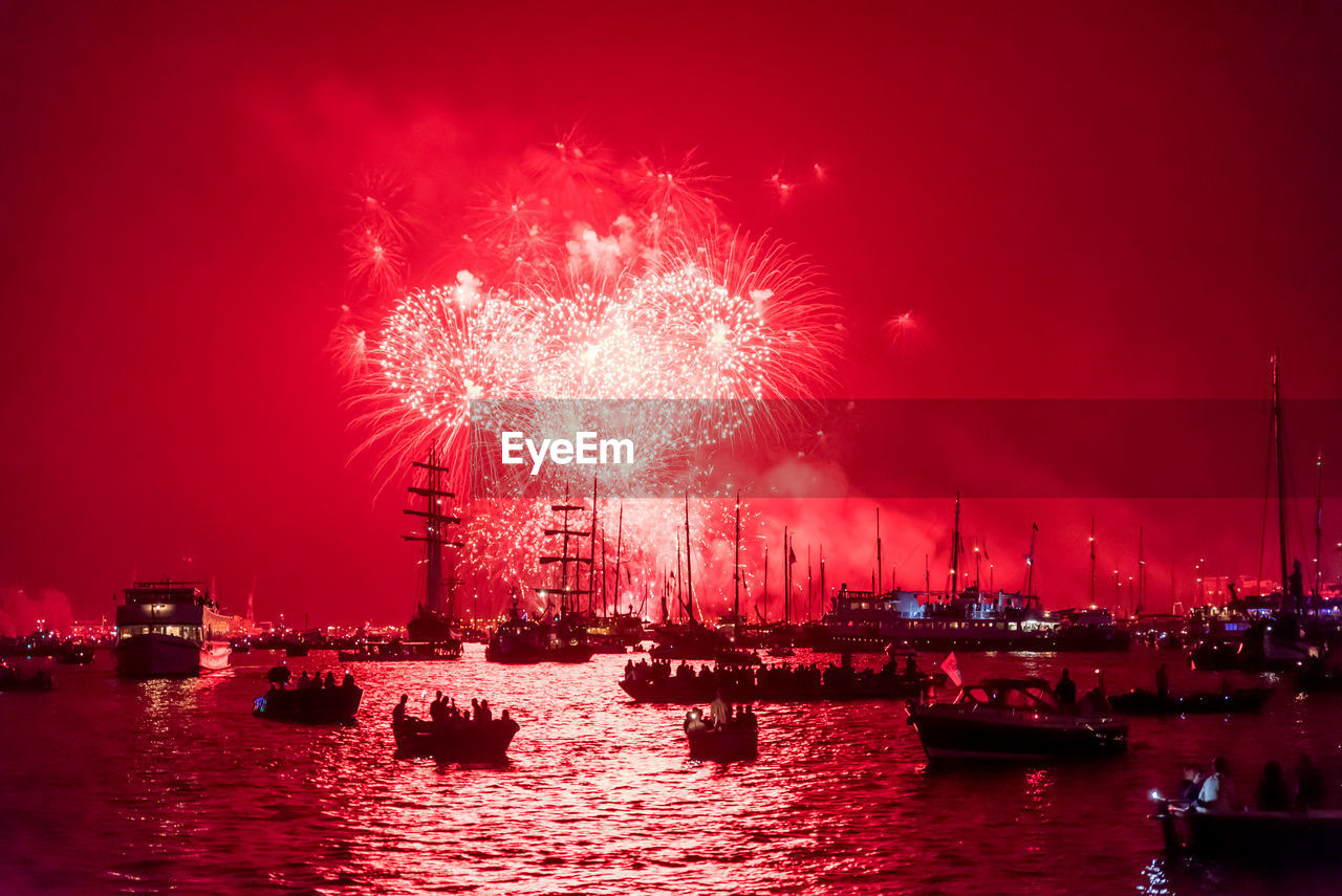 Firework display by river against sky